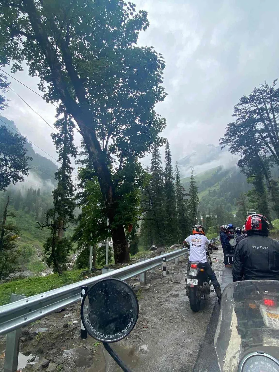 Riders on motorcycles on a wet mountain road in the rain, pine trees and cloud above