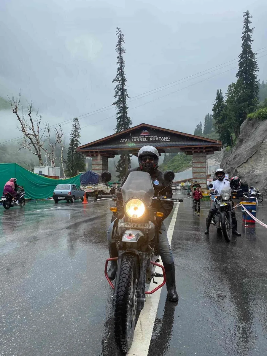 A rider in a helmet and rain jacket on a motorcycle at a mountain checkpost, riders behind