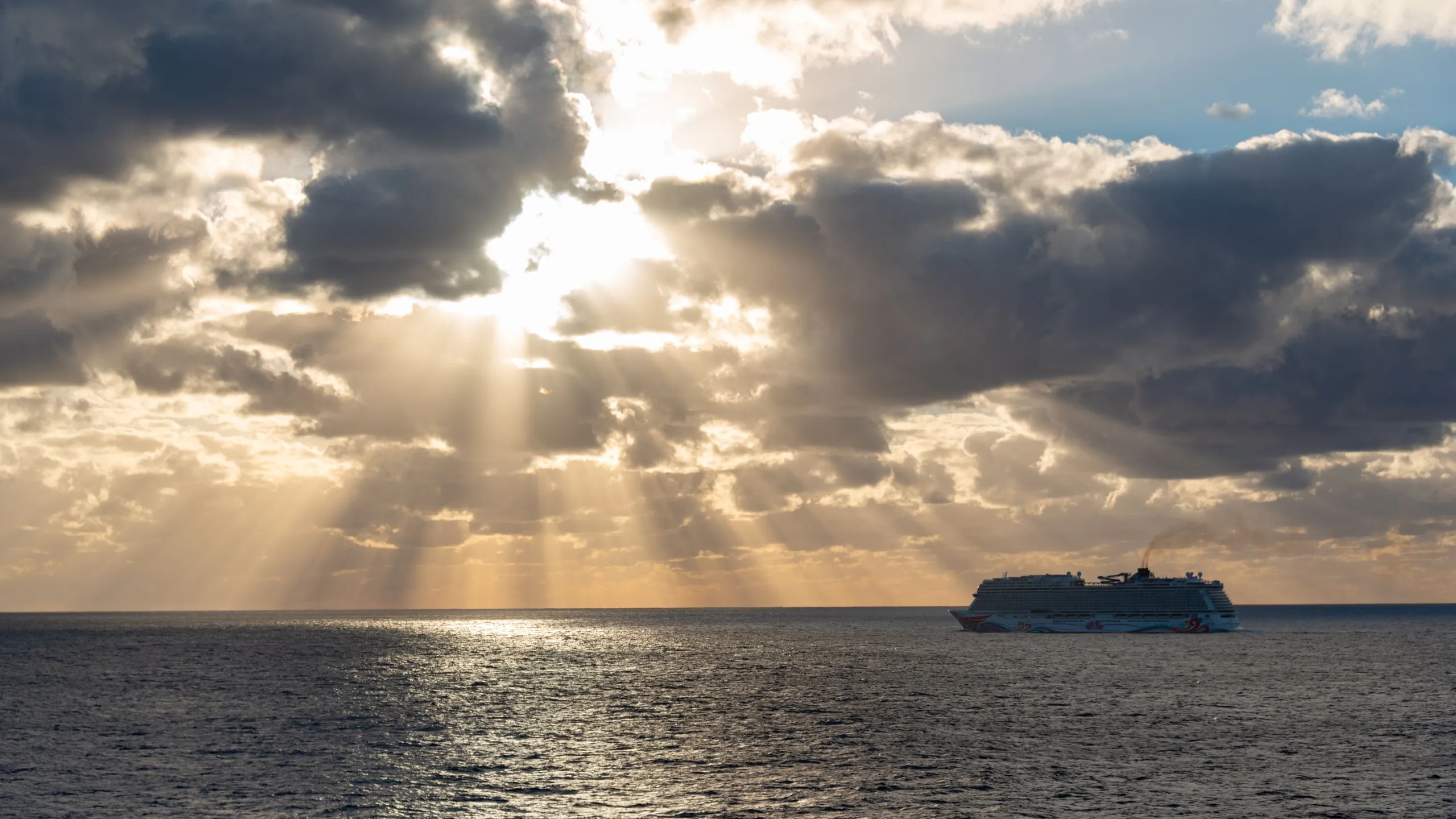 Sun rays through clouds over the sea, a cruise ship on the horizon