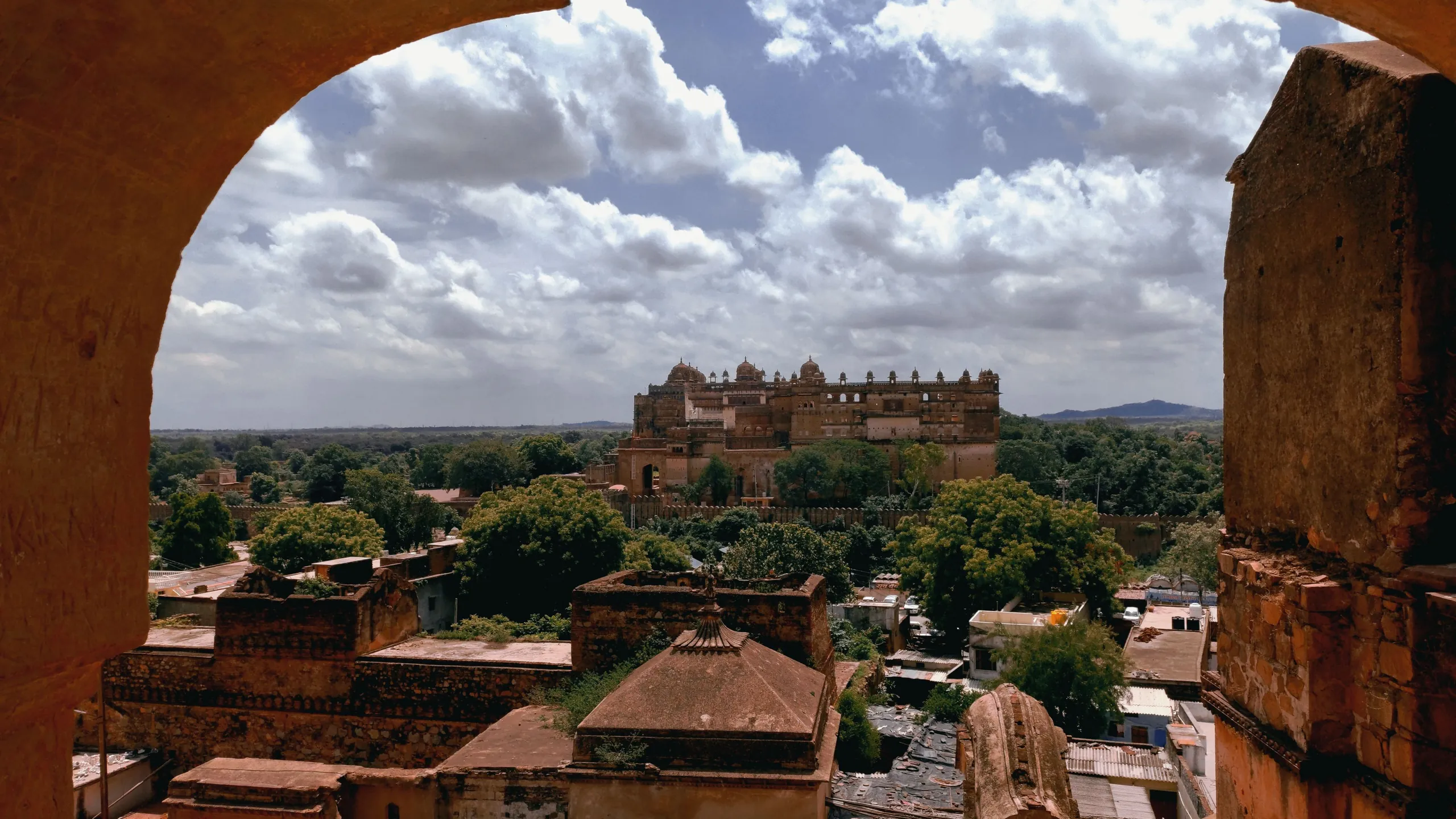 The fort at Orchha seen through a stone arch, clouds above