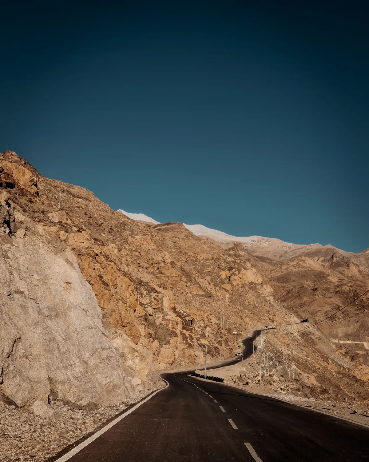 A mountain road leading into bare Himalayan hills under a dark blue sky