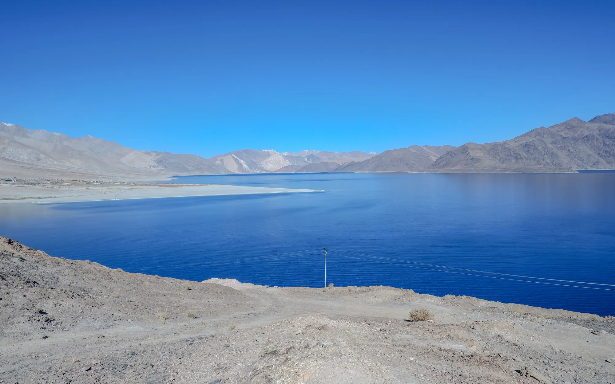 A gravel track leading down to the blue water of Pangong lake, Ladakh, mountains beyond