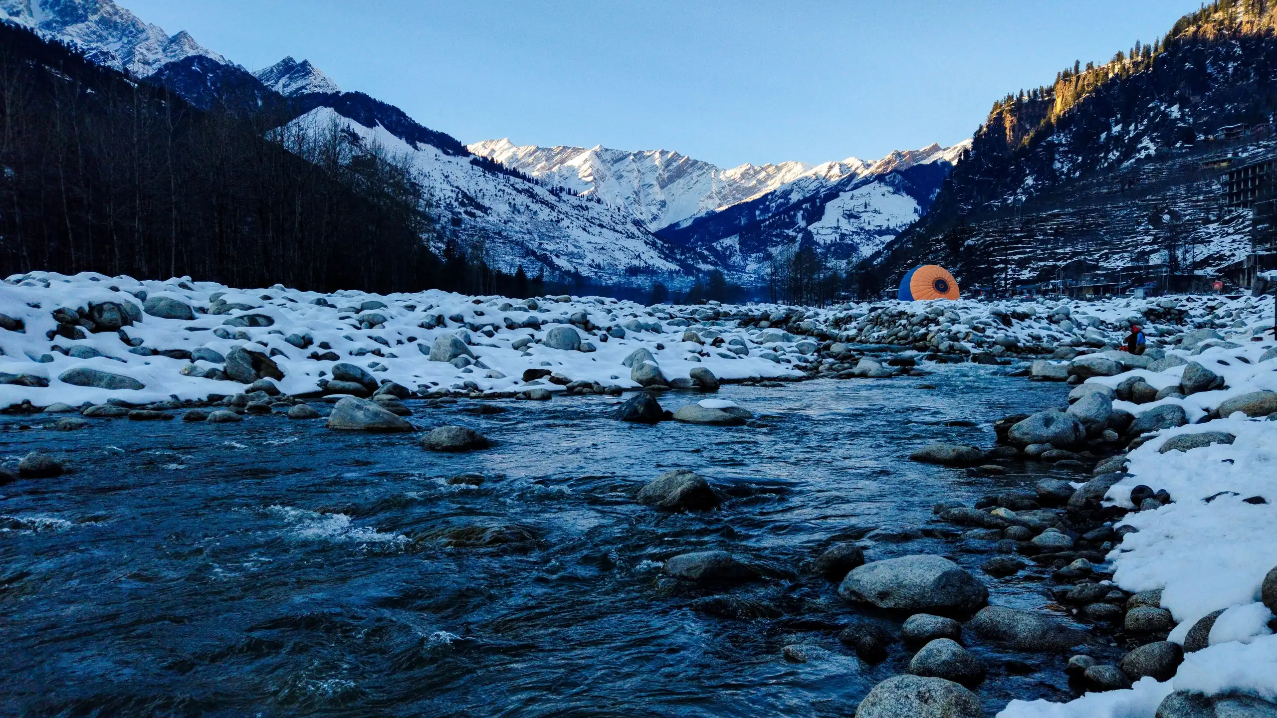 The Beas river running over snowy stones below the mountains at Manali