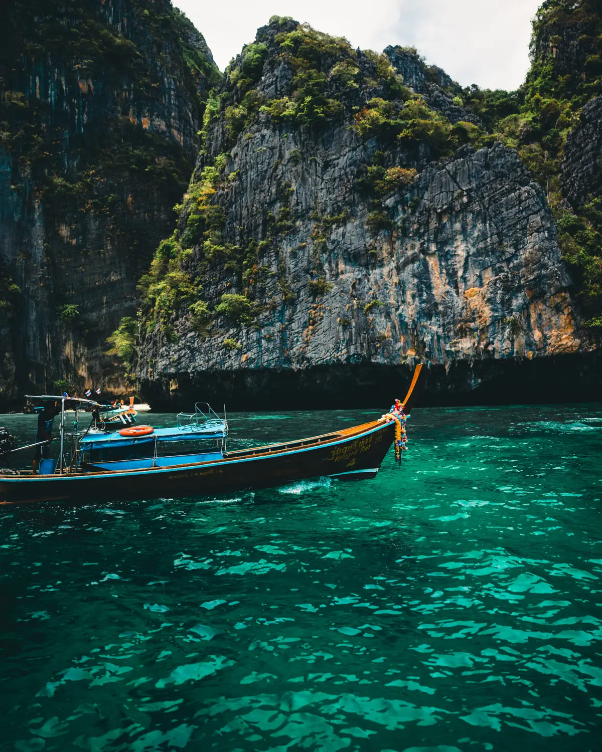 A long-tail boat on the green sea below limestone cliffs in Thailand