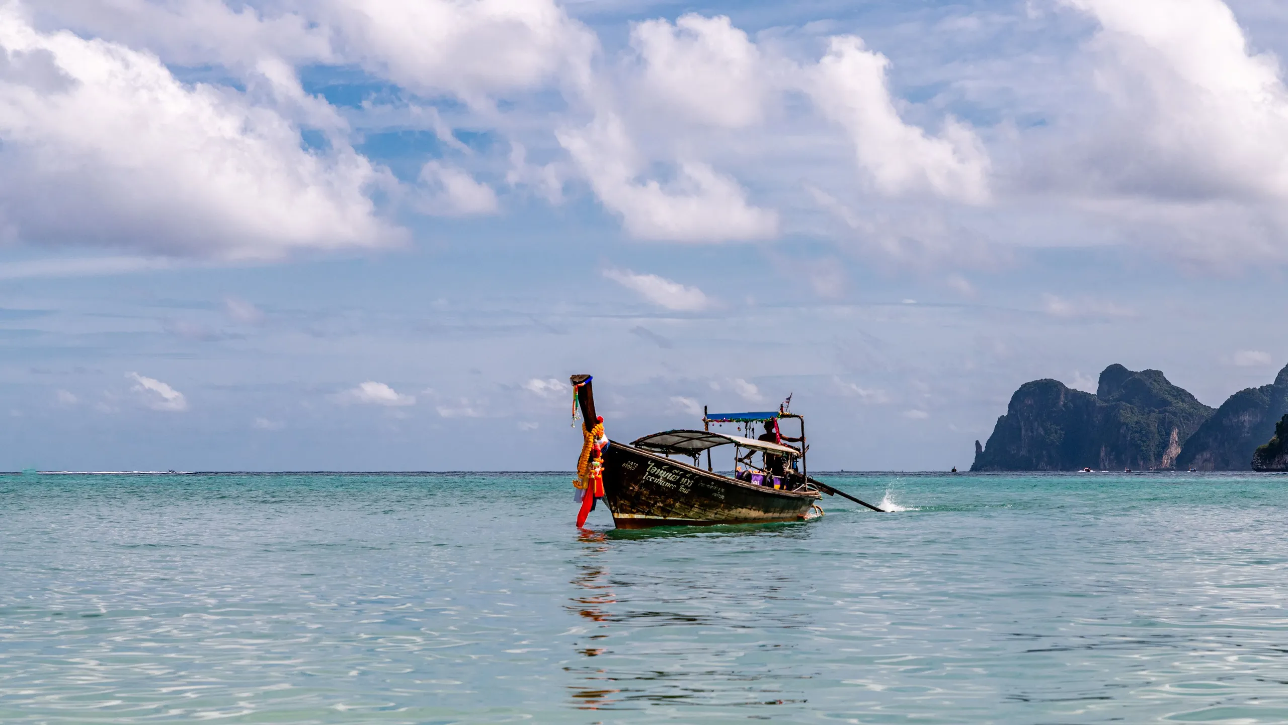 A long-tail boat on the calm sea off Phuket, Thailand, clouds above